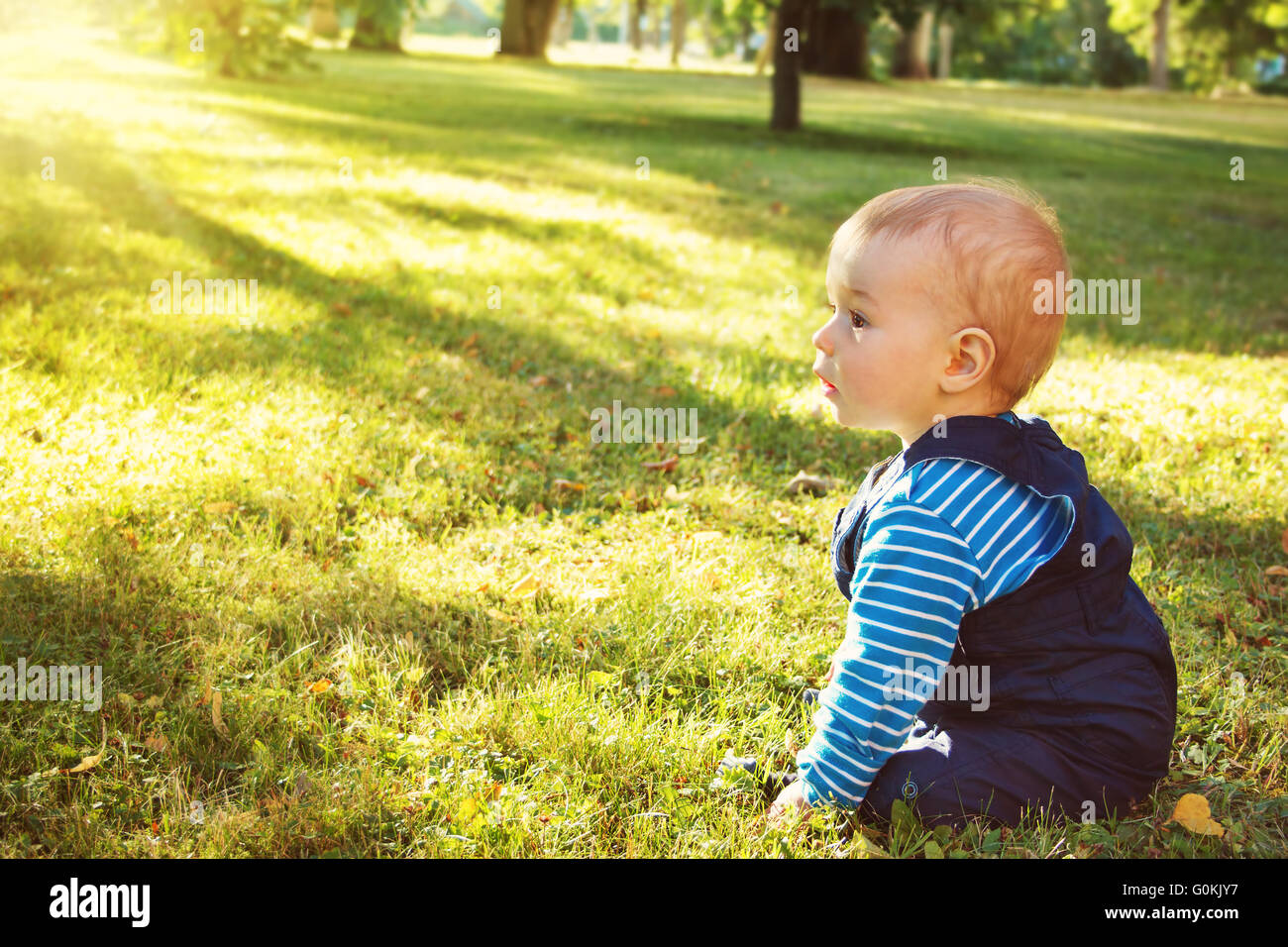 Piccolo Ragazzo seduto nel parco Foto Stock