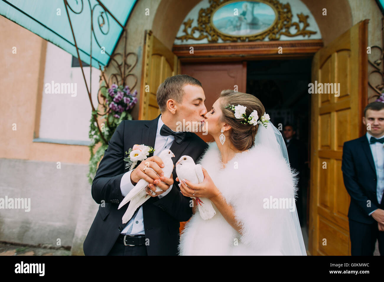 Happy sposi sposa e lo sposo con le colombe in mani sulle porte della chiesa sullo sfondo Foto Stock