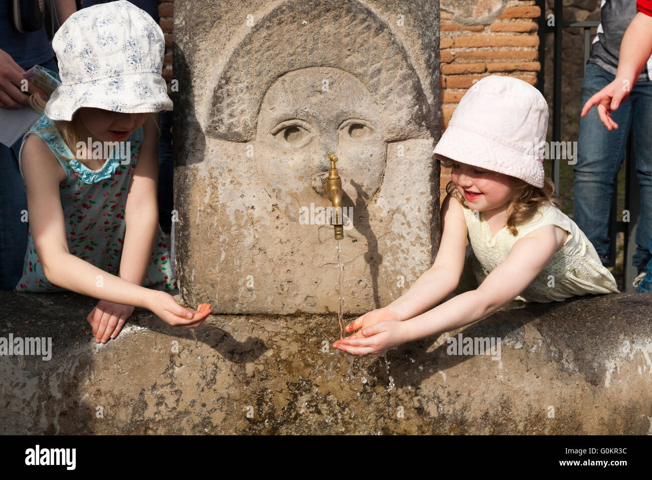 Turisti turistiche bambini kid kids drink / bere da una pubblica fontana di acqua di rubinetto in Roman Pompei Pompei. Napoli Italia Foto Stock