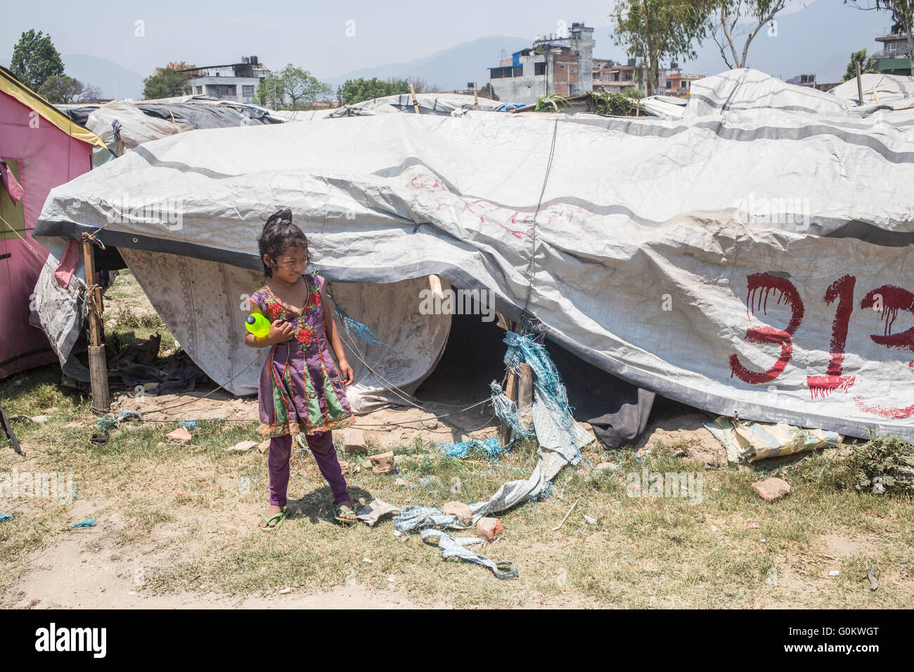 Bambino in piedi con una bottiglia di acqua accanto a una tenda rotto in un terremoto camp istituito nel 2015 a Kathmandu. Foto Stock