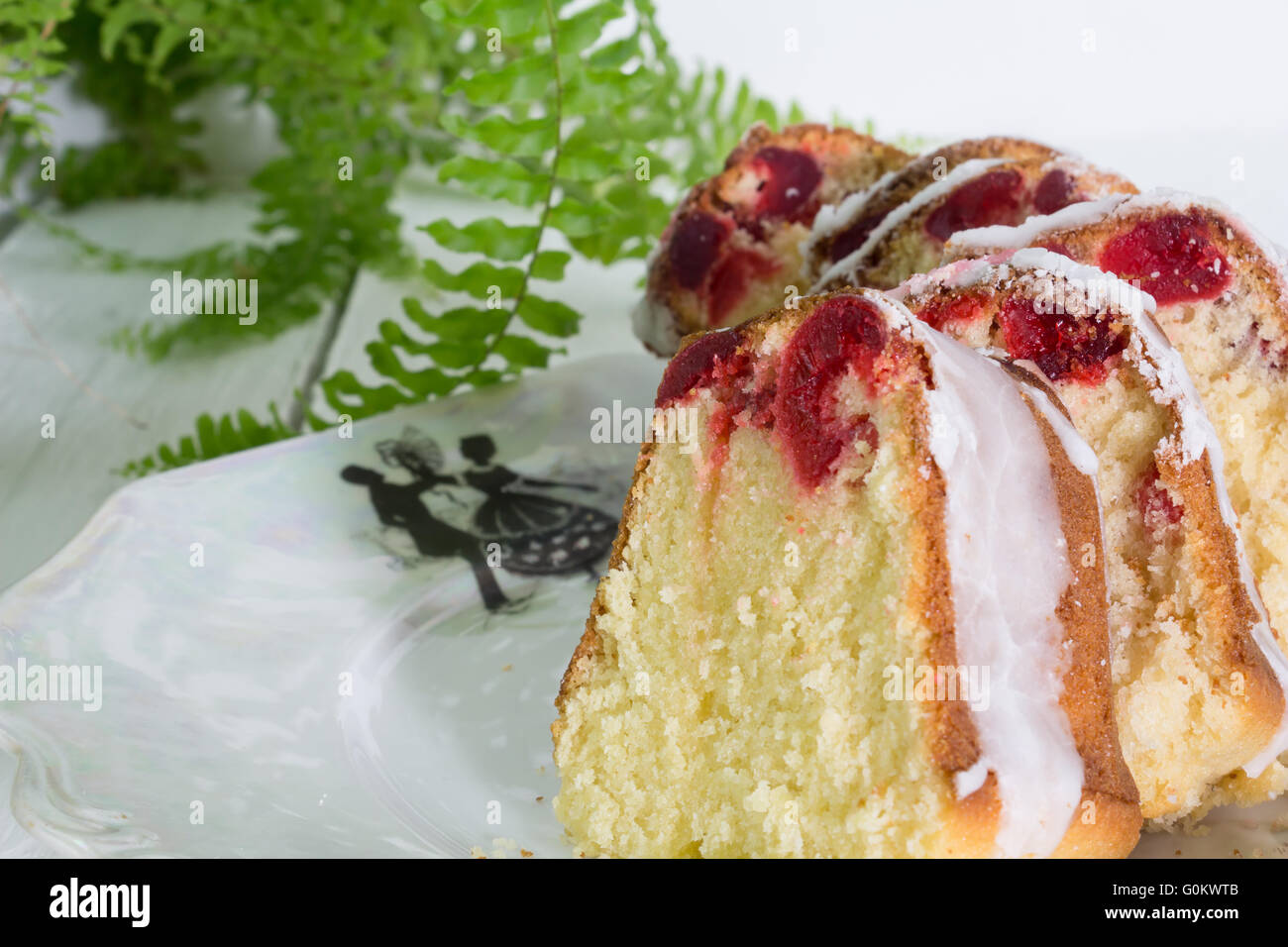 Primo piano di fette di vetri ciliegia sulla torta vintage piastra bianca con Boston fern sulla tavola di legno Foto Stock