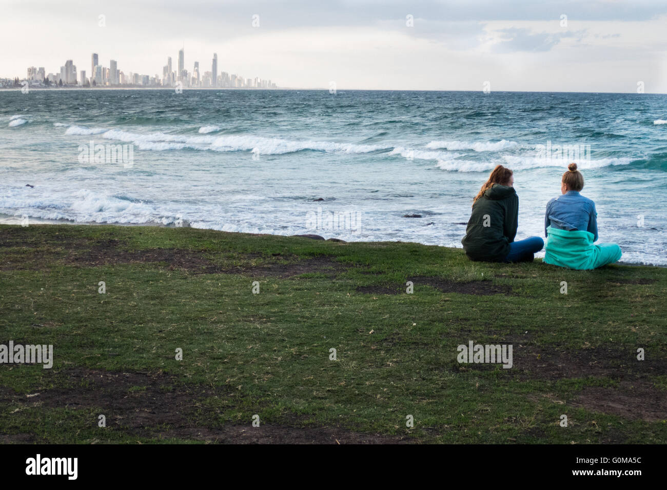 Due giovani donne seduta che si affacciano sull'Oceano Pacifico a Burleigh capi nel Queensland in Australia. Foto Stock