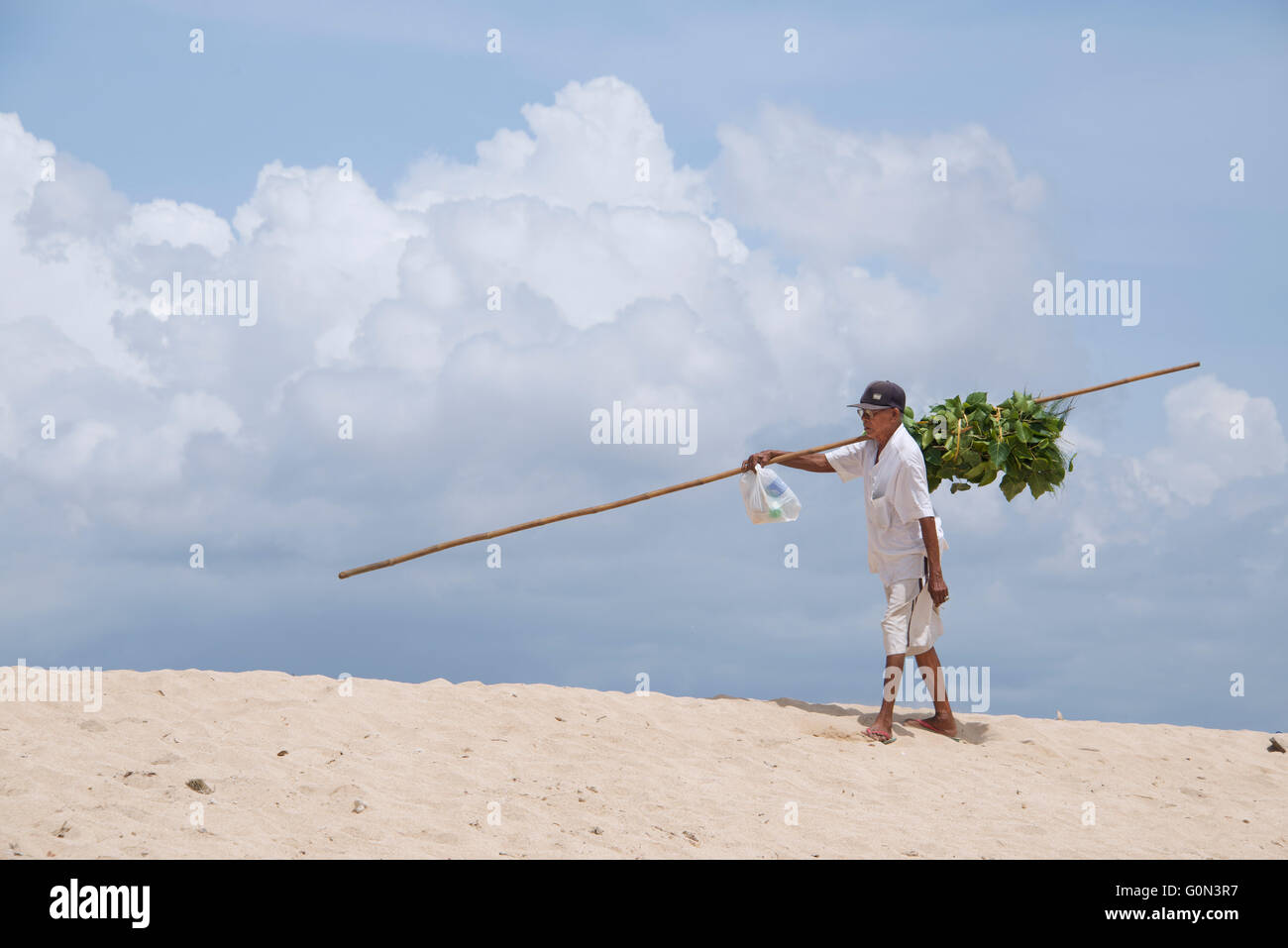 Uomo che porta verdure commestibili in pole la spiaggia di Nusa Dua Bali Indonesia Foto Stock