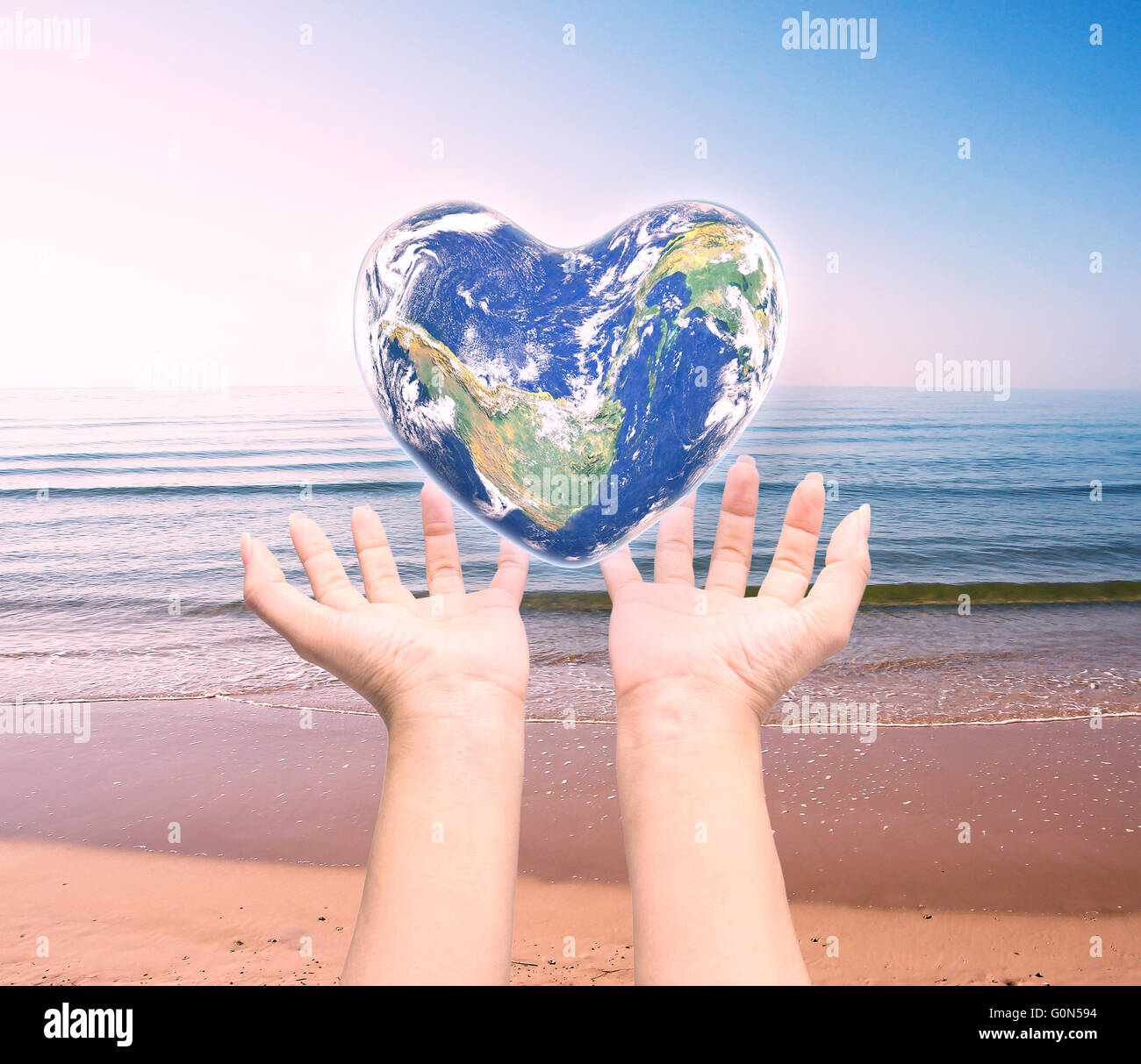 Mondo in forma di cuore con sopra le donne le mani umane su sfocato sfondo naturale: Mondo Salute del cuore giorno,Elemento di questa immagine fur Foto Stock