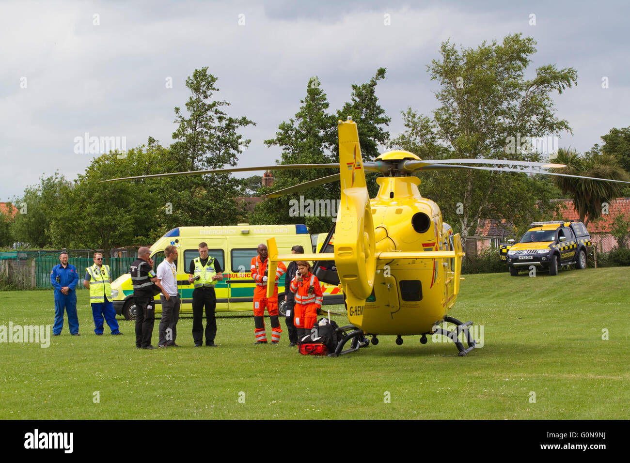 East Anglia Air Ambulance in un campo contenente una strada ambulanza e guardia costiera veicolo con un sacco di personale di emergenza Foto Stock