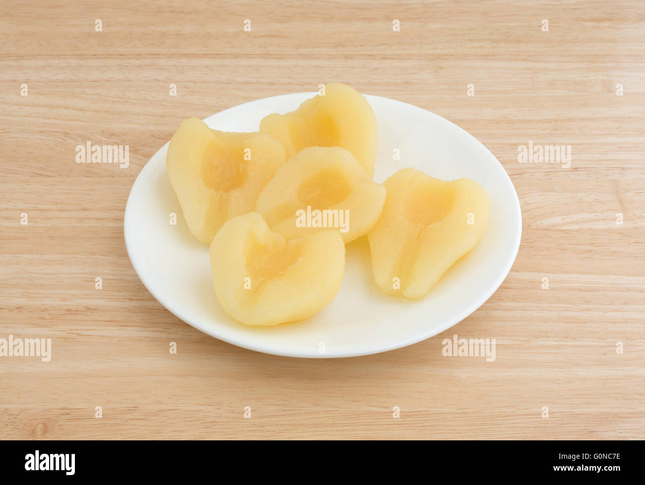 Vista laterale di diverse metà di pera su una piastra bianca in cima a una tavola di legno alto. Foto Stock
