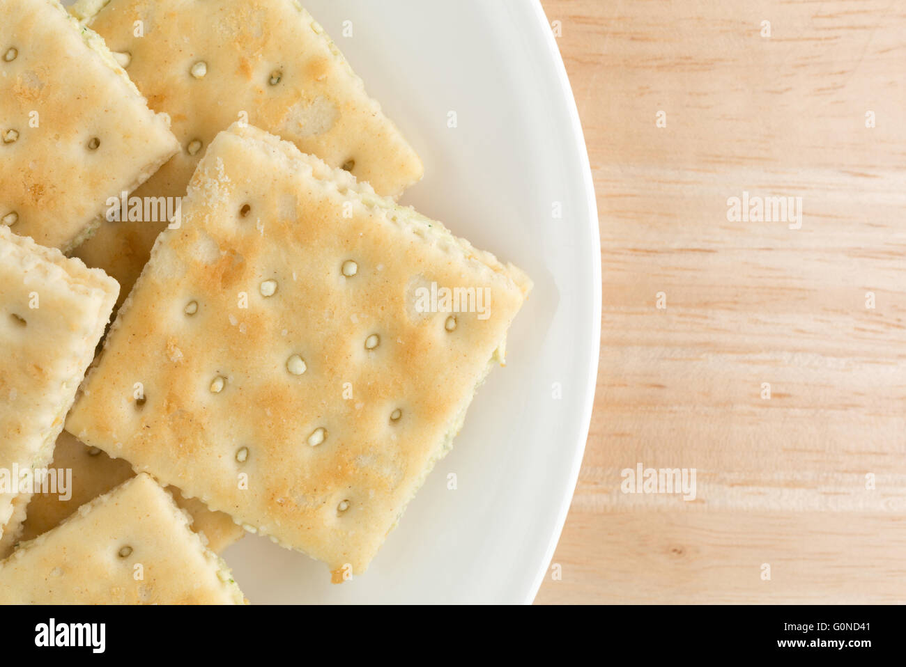 Top vista ravvicinata della crema di formaggio e cracker di erba cipollina su una piastra bianca in cima a una tavola di legno alto. Foto Stock