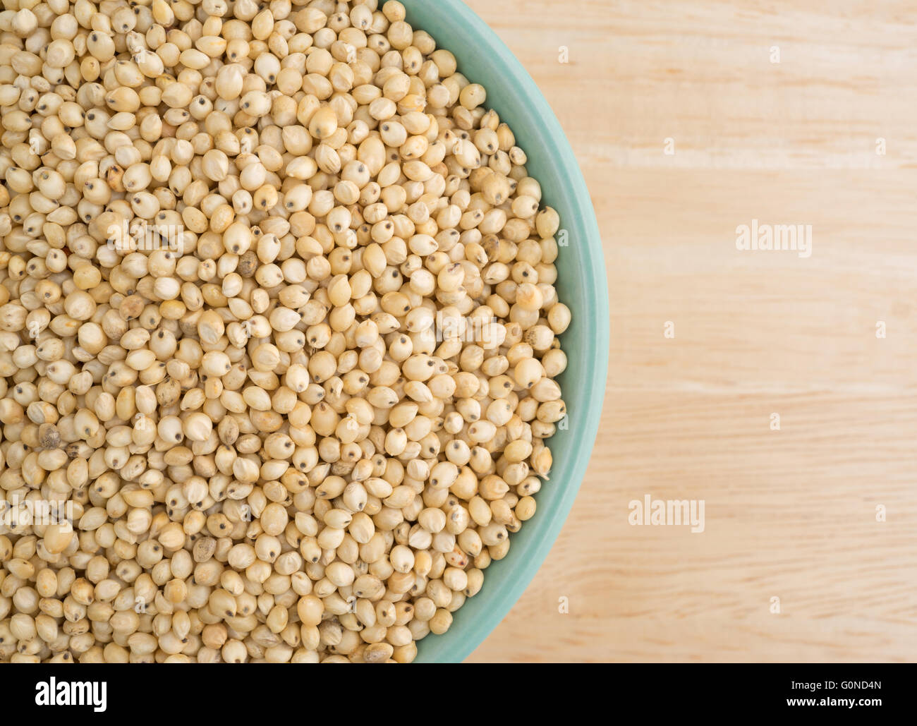 Top vista ravvicinata di una piccola ciotola riempita con grano intero organico semi di sorgo su una tavola di legno alto. Foto Stock