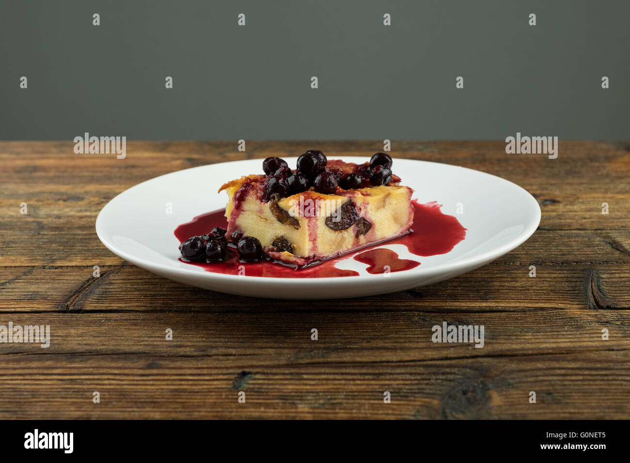 Il budino con le prugne secche, le uve secche di Corinto sulla parte superiore di una piastra bianca su una tavola di legno Foto Stock