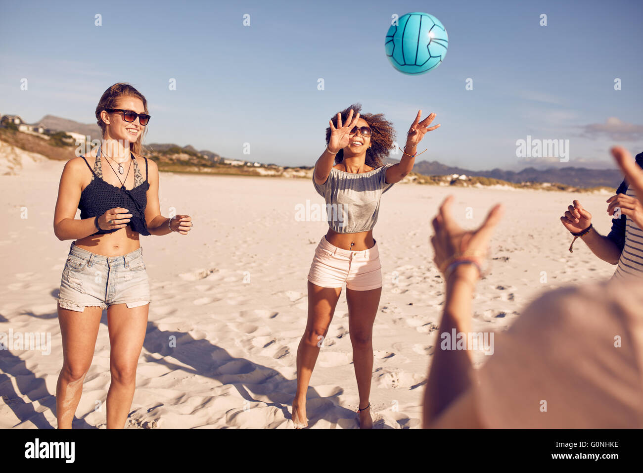 Ritratto di giovane donna giocando a pallavolo con gli amici sulla spiaggia. Gruppo di amici giocando a pallavolo. Foto Stock