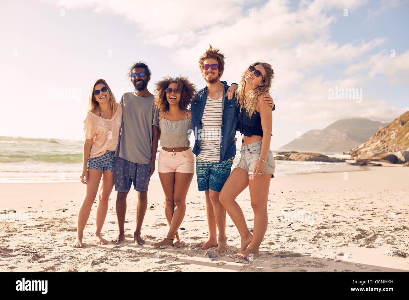 Gruppo di amici in piedi insieme ad una spiaggia un giorno d'estate. Felice giovani godendo una giornata in spiaggia. Foto Stock