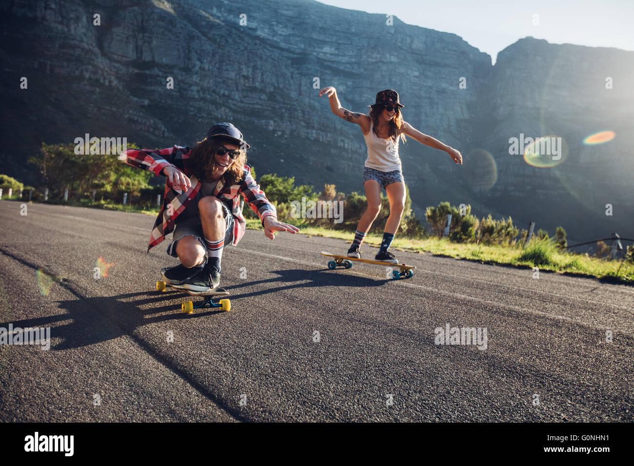 Felice giovani amici divertendosi con lo skateboard. Giovane uomo e donna pattinaggio insieme in una giornata di sole. Foto Stock
