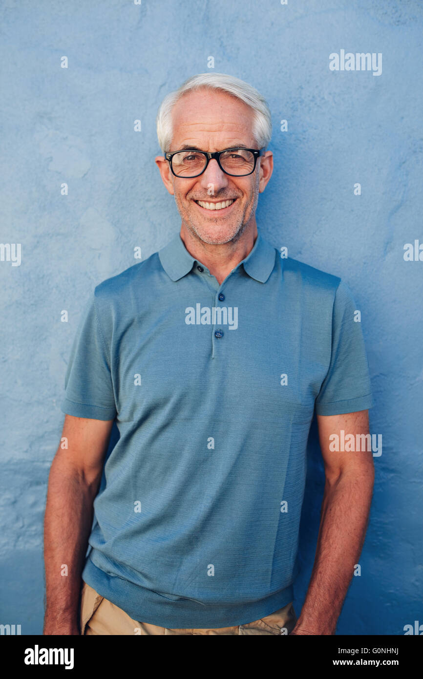Ritratto di bello uomo maturo con gli occhiali guardando la fotocamera e sorridente, egli è appoggiata contro una parete di blu. Foto Stock