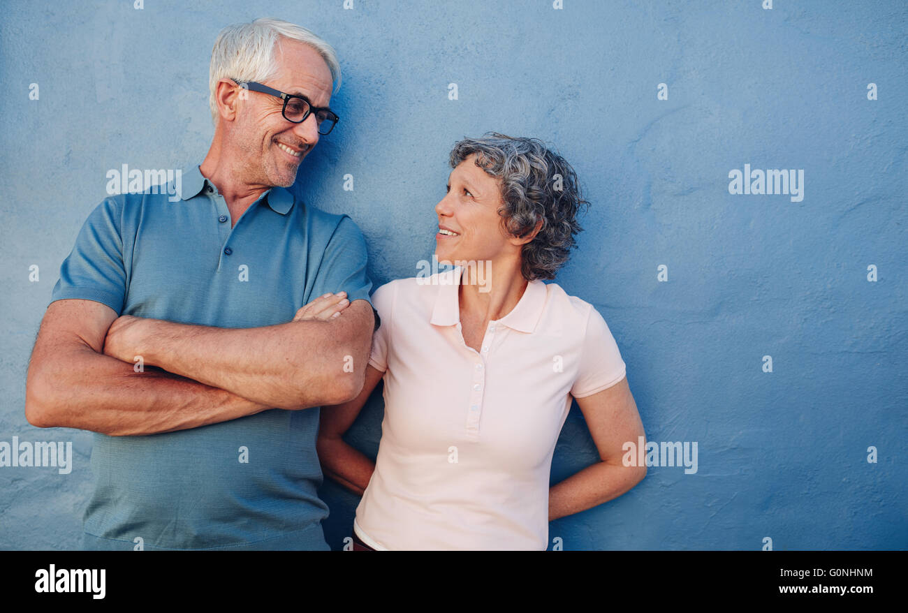 Ritratto di affettuosa coppia matura guardando ogni altra contro sfondo blu. Amare medio di età compresa tra uomo e donna in piedi Foto Stock