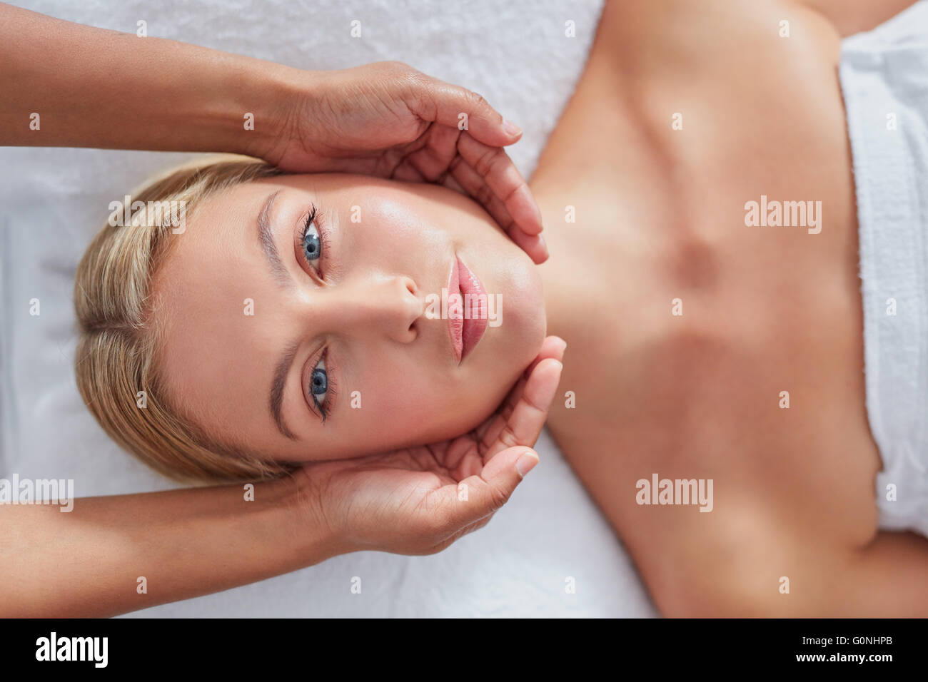 Immagine ravvicinata di bella giovane donna avente un massaggio del viso a health spa. Faccia caucasica e massaggiatrice mani. Foto Stock
