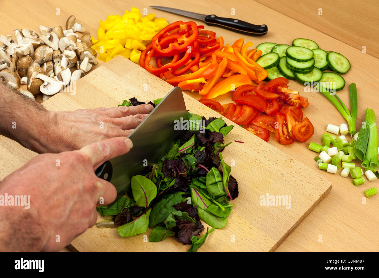 Lo Chef chopping babyleaf alcune foglie di insalata con una mannaia coltello su un tagliere di legno a parte alcune verdure miste Foto Stock