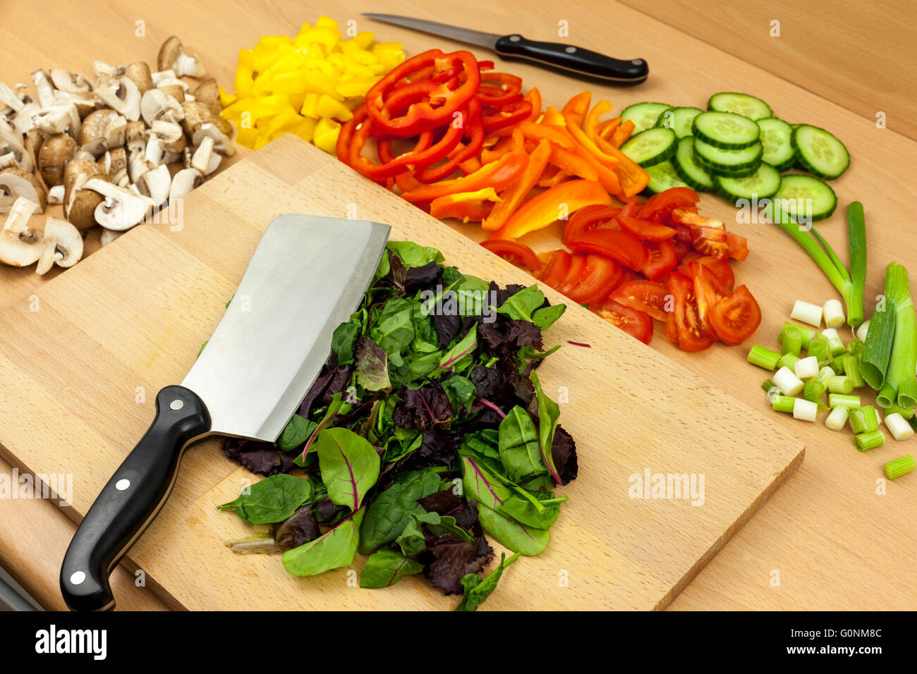 Cleaver coltello posa sulla cima di alcune appena tagliate insalata babyleaf su di un tagliere a parte una selezione di altri ortaggi e legumi Foto Stock