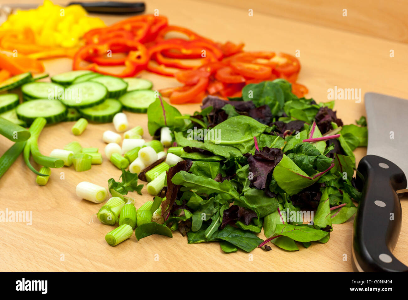 Immagine ravvicinata di alcuni baby insalata in foglie e una mannaia alonge coltello lato una selezione di altre verdure tritate Foto Stock