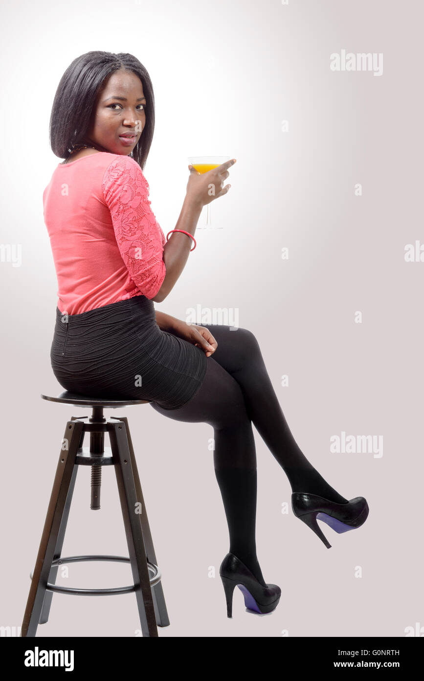 Una bella donna africana di bere succo di arancia, seduti su uno sgabello Foto Stock