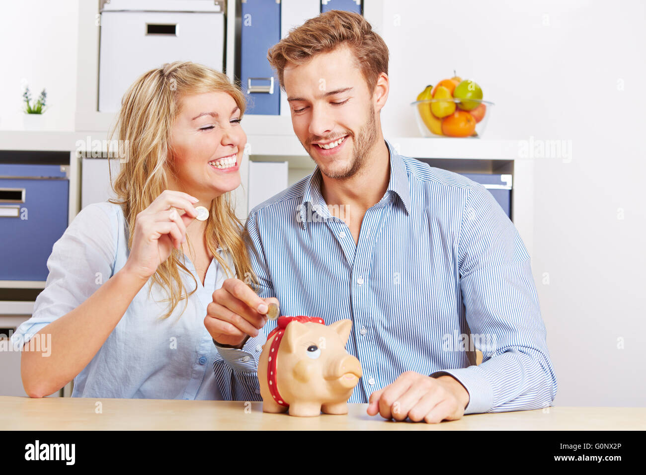 Coppia felice mettendo mony Euro monete in un salvadanaio Foto Stock