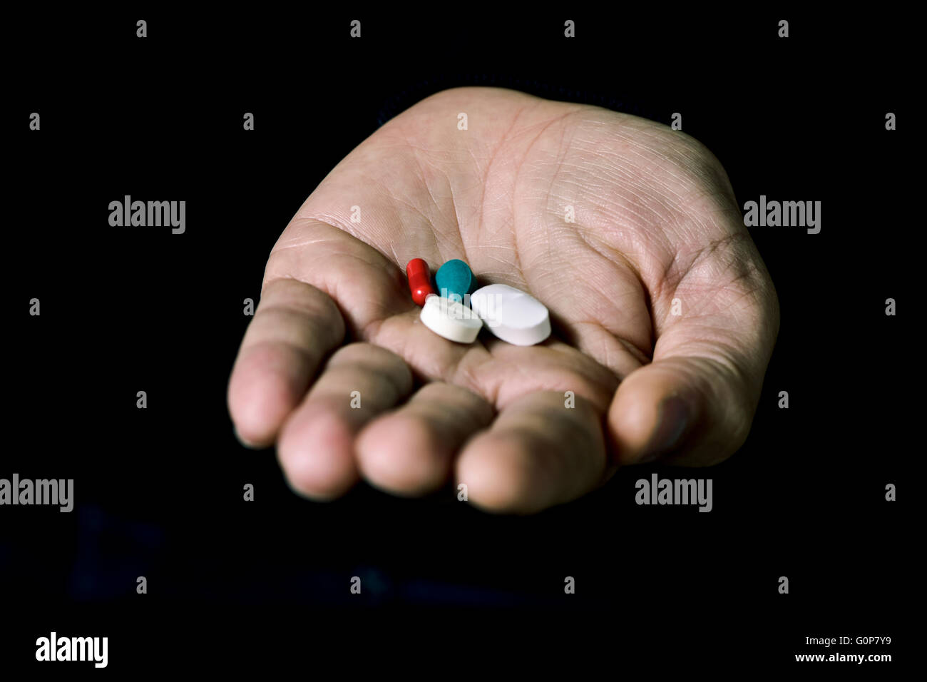 Primo piano della mano di un uomo giovane con alcune pillole diverse su uno sfondo nero Foto Stock