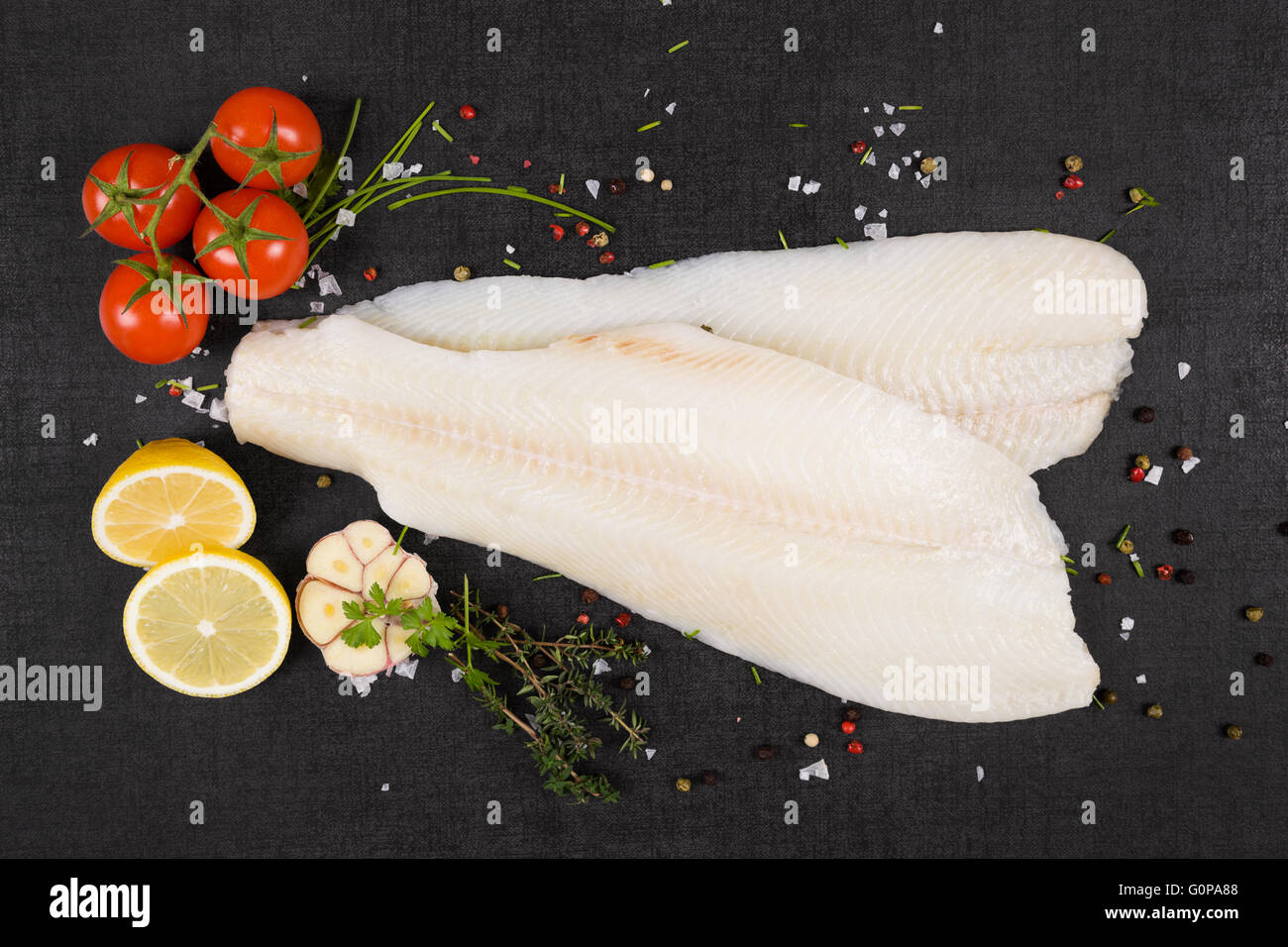 Fresco di filetto di halibut con erbe fresche e aglio sul nero scuro dello sfondo in pietra vista dall'alto. Lussuoso mangiare pesce sfondo. Foto Stock