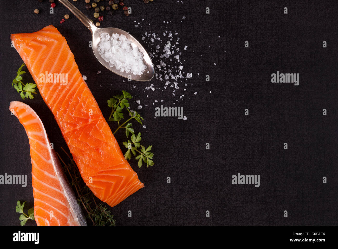 Sfondo di salmone con copyspace. Bistecca di salmone, limone, rosmarino e foglie di prezzemolo e sale su sfondo nero, piatto laici. Foto Stock