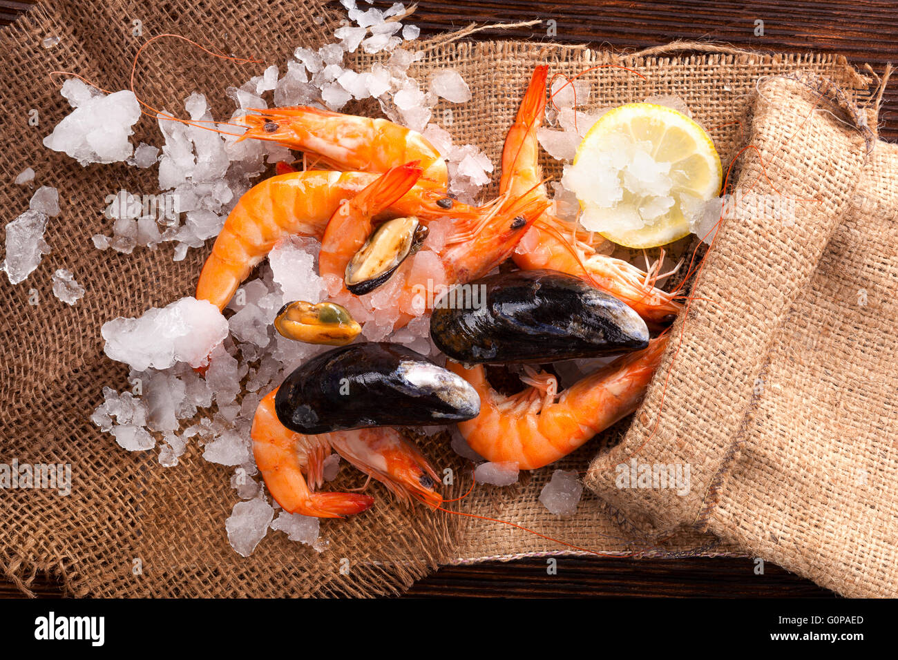 Gamberi freschi con limone sul ghiaccio in marrone borsa di tela su tavola di legno, vista dall'alto. Culinario mangiare pesce. Foto Stock
