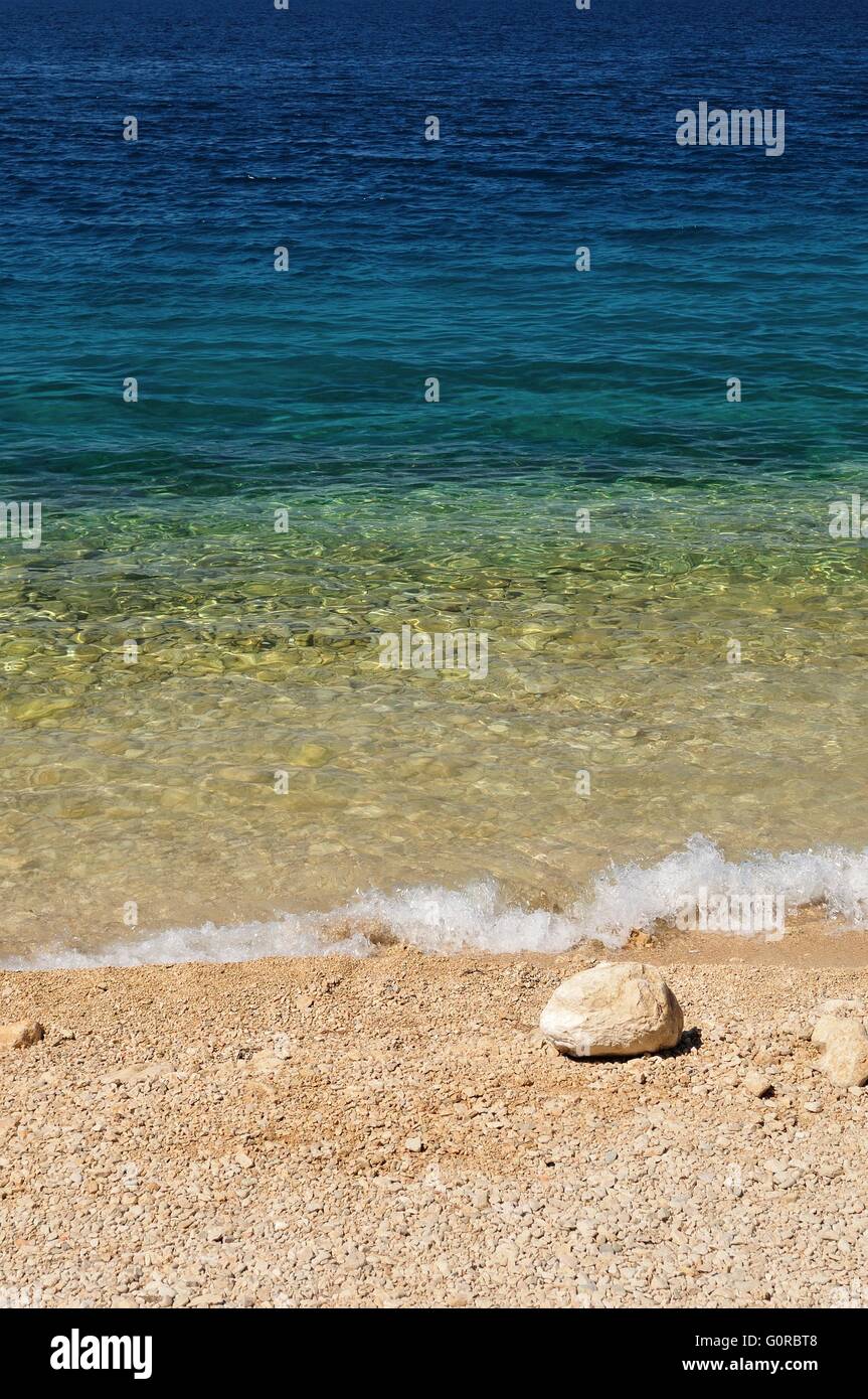 Bellissima spiaggia con onde e big stone nel lato inferiore destro della foto. Podgora, Croazia Foto Stock