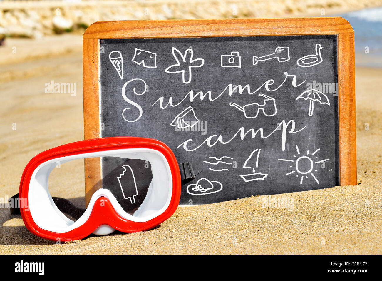Alcuni disegni di roba estiva e il testo Summer Camp scritto su una lavagna  posta sulla sabbia di una spiaggia accanto a un rosso e w Foto stock - Alamy
