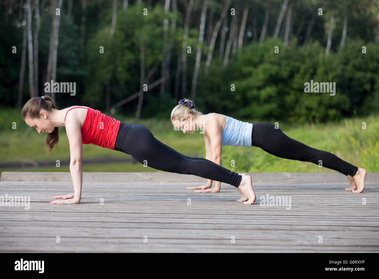 Montare due giovani belle donne che lavorano fuori all'aperto nel parco sulla giornata estiva, indossare abbigliamento sportivo di rosso e di blu canotte, facendo plank Foto Stock
