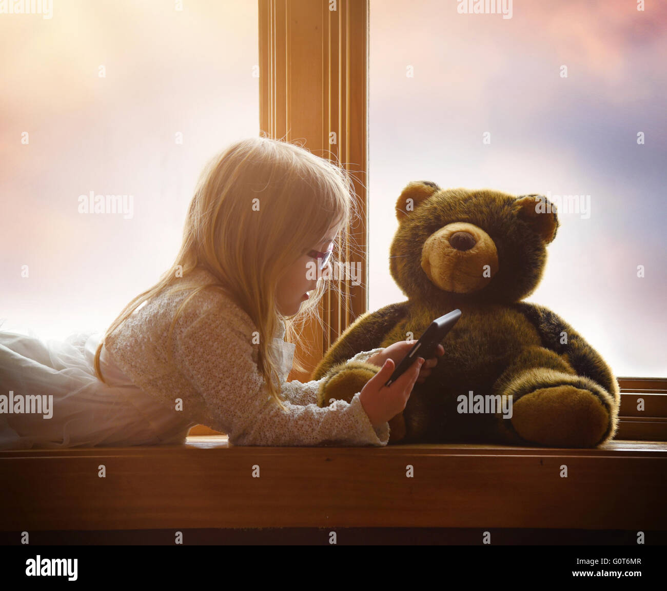 Un bambino sta giocando con una tavoletta elettronica in una finestra con il suo orsacchiotto di peluche per un gioco, app o il concetto di intrattenimento. Foto Stock