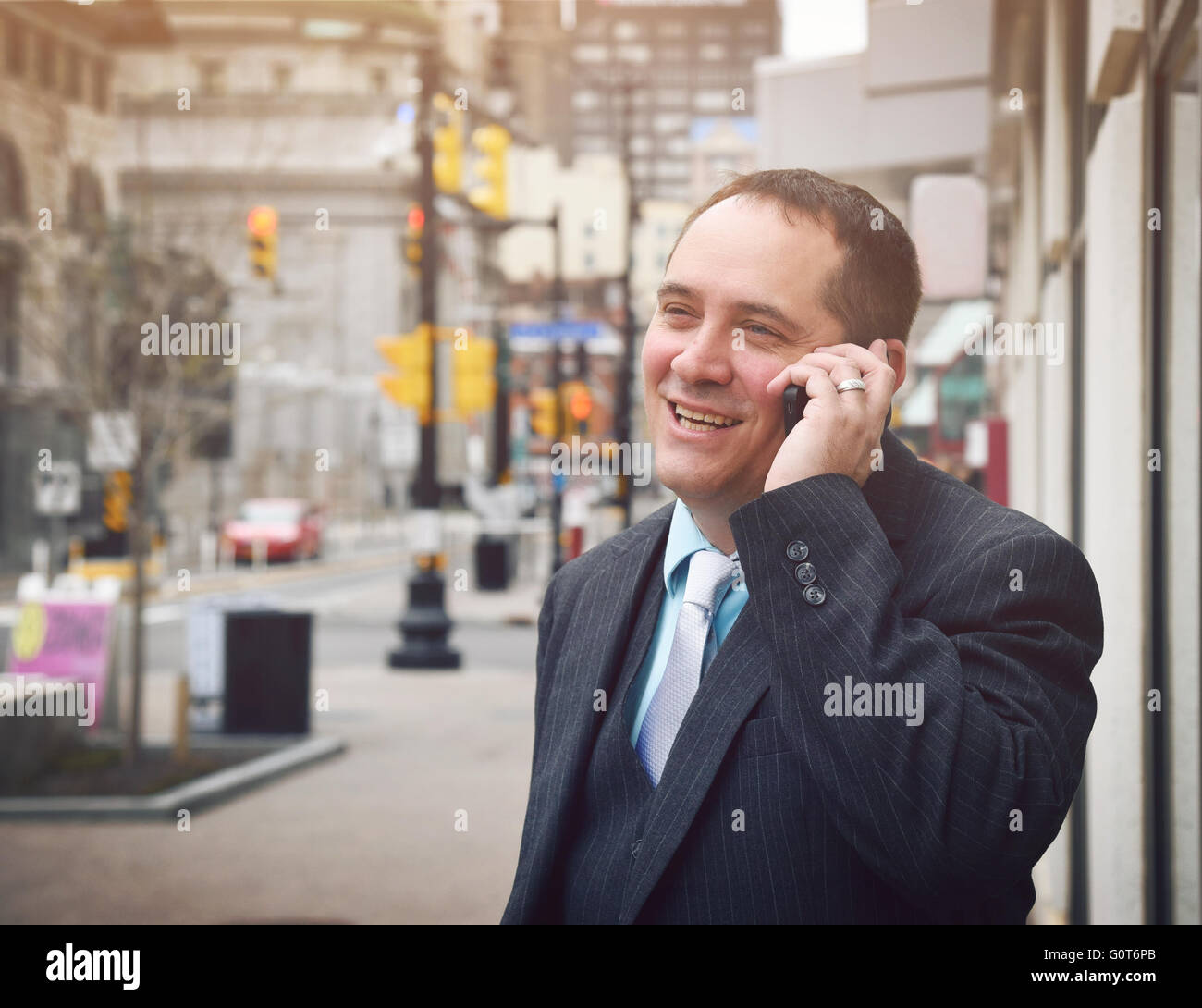 Un uomo d'affari sta parlando su un telefono cellulare al di fuori di una città che indossa una tuta e sorridere per un successo o un idea di comunicazione Foto Stock