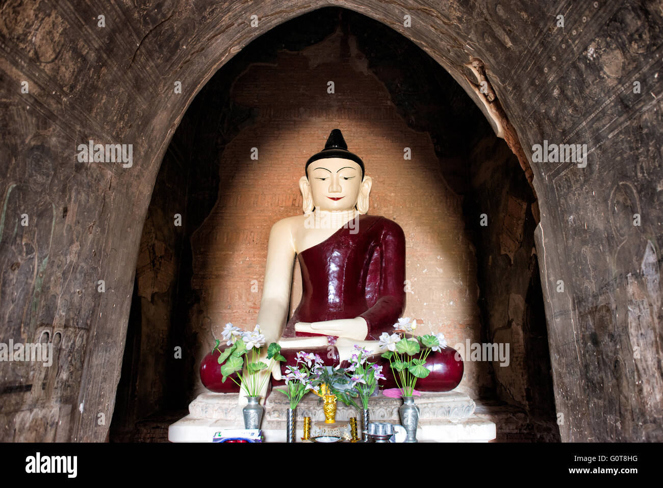 Tempio di Tayok Pye, statua del Buddha Bagan Myanmar // BAGAN, Myanmar - Una grande statua di Buddha con un profondo abito rosso si trova all'interno del santuario principale del Tempio di Tayok Pye, circondato da affreschi ben conservati che coprono le pareti e il soffitto della camera ad arco. Risalente al regno di re Narathihapate (1256-1287), il tempio di Tayok Pye si trova sul lato orientale della zona archeologica di Bagan vicino al villaggio di Minnanthu. Il tempio rappresenta la fase finale della costruzione monumentale prima che le invasioni mongole precipitassero il declino del regno pagano. La struttura è caratterizzata da intricati stucc rinnovati Foto Stock