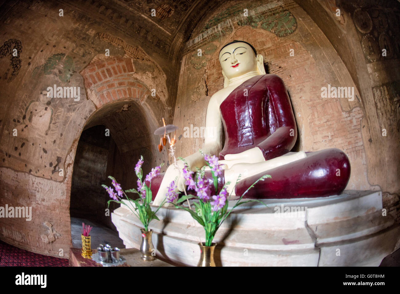 Tempio di Tayok Pye, statua del Buddha Bagan Myanmar // BAGAN, Myanmar - Una grande statua di Buddha con un profondo abito rosso si trova all'interno del santuario principale del Tempio di Tayok Pye, circondato da affreschi ben conservati che coprono le pareti e il soffitto della camera ad arco. Risalente al regno di re Narathihapate (1256-1287), il tempio di Tayok Pye si trova sul lato orientale della zona archeologica di Bagan vicino al villaggio di Minnanthu. Il tempio rappresenta la fase finale della costruzione monumentale prima che le invasioni mongole precipitassero il declino del regno pagano. La struttura è caratterizzata da intricati stucc rinnovati Foto Stock