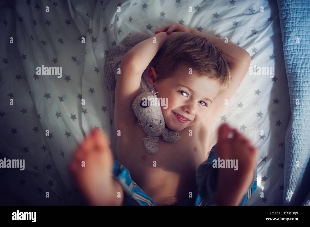 Sorridente ragazzo disteso sul letto con peluche Foto Stock