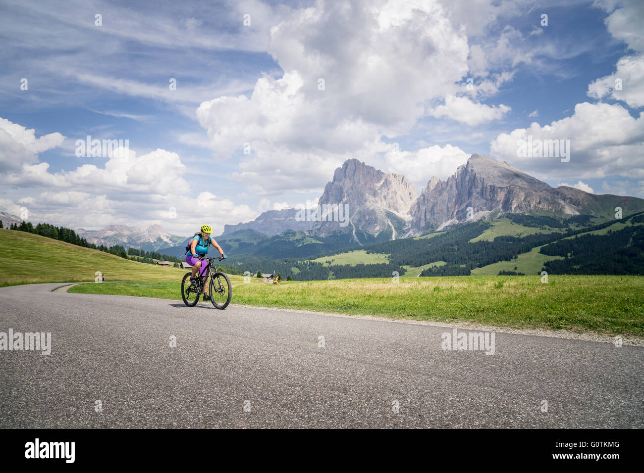 Una donna equitazione mountain bike lungo la strada in Dolomiti, Val Gardena, Italia Foto Stock