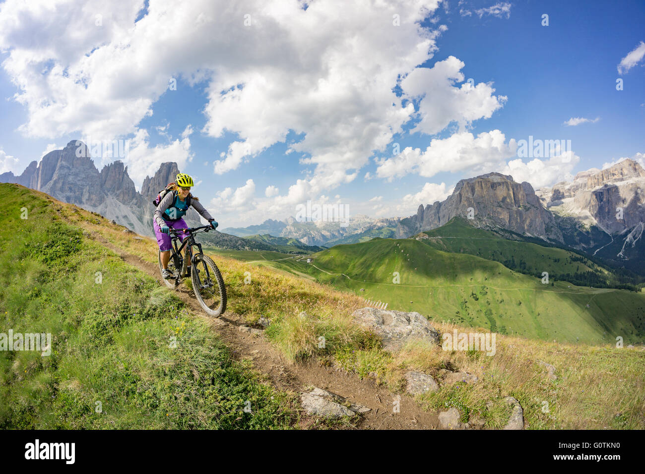 Una donna equitazione mountain bike lungo la strada in Dolomiti, Val Gardena, Italia Foto Stock