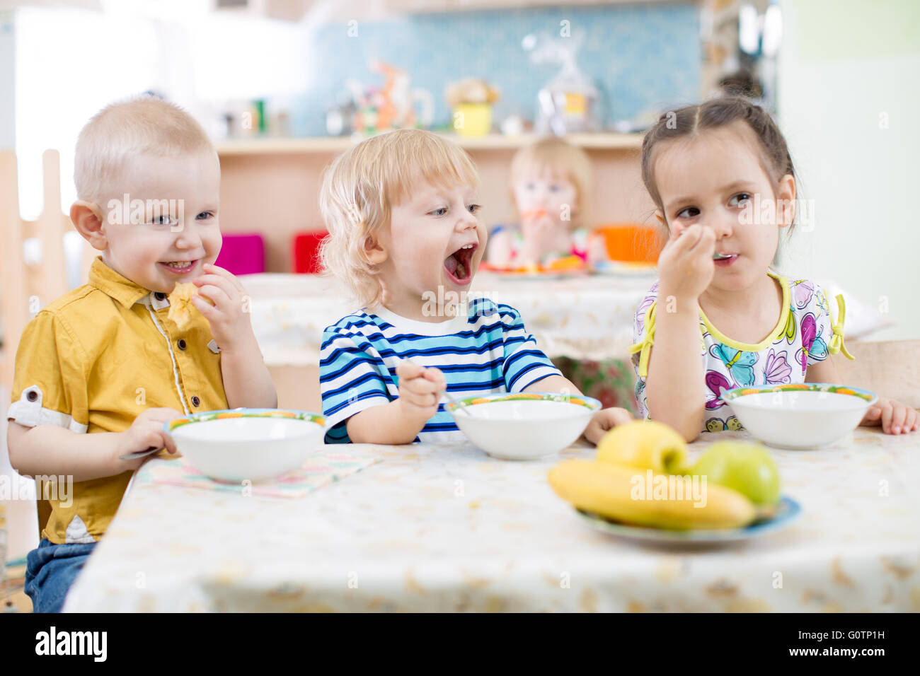 Funny ragazzino con bocca aperta a mangiare nella scuola materna di gruppo Foto Stock