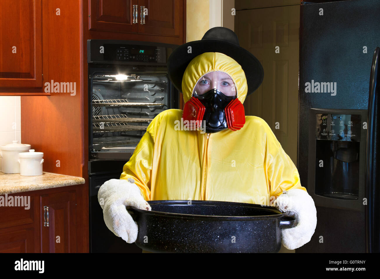 La donna in giallo HazMat suit e indossare il respiratore pellegrino hat in piedi accanto ad aprire il forno in cucina. Foto Stock