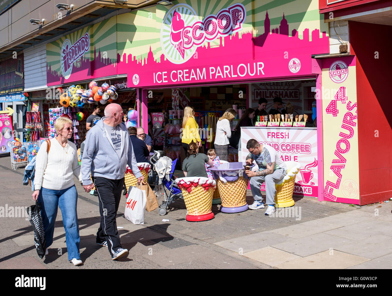 Un giovane a piedi passato persone godendo di gelato presso il convogliatore gelateria sul lungomare di Blackpool, Lancashire, Regno Unito Foto Stock