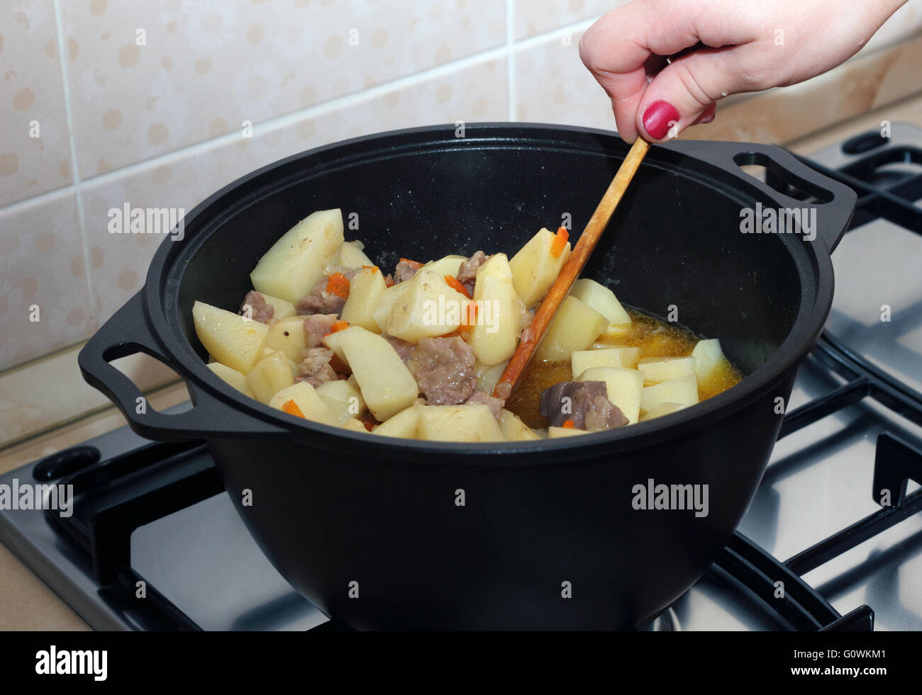 Donna di mano mescolando stufati di patate con la carne in metallo nero pot Foto Stock