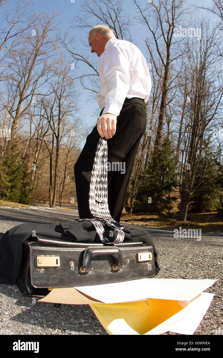 Imprenditore valigetta di caduta e la rimozione di giacca e cravatta come egli colpisce la strada, concetto di pensionamento Foto Stock