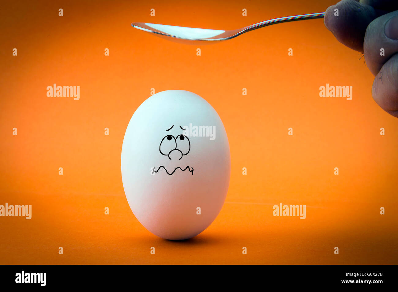 Incrinatura della testa di uovo su sfondo arancione. Spaventata uovo guardando a cucchiaio. Foto Stock