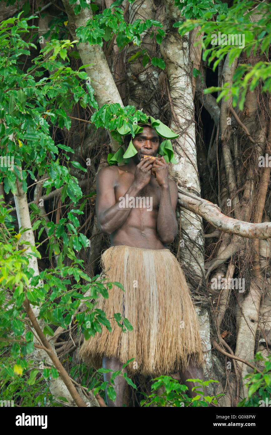 Uomo in abito tradizionale svolge flauto in arti di strangler fig tree, dell'isola di Tanna, Vanuatu Foto Stock