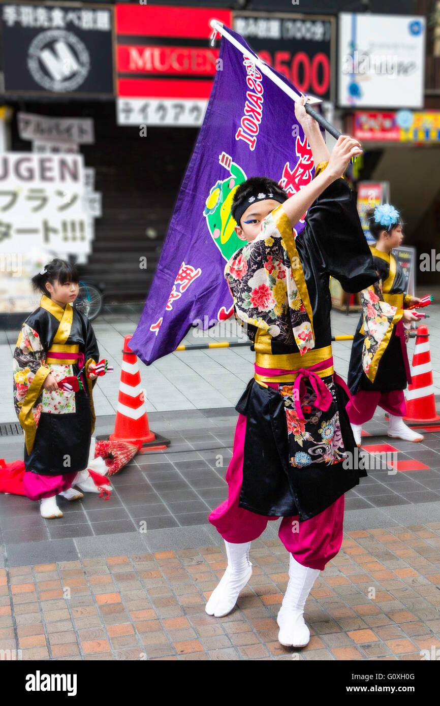 Yosakoi giapponese festival. Due giovani ragazzi, ragazze, in costume di danza, yukata, con il vecchio ragazzo di fronte di vorticazione viola grande bandiera durante spettacoli di danza. Foto Stock