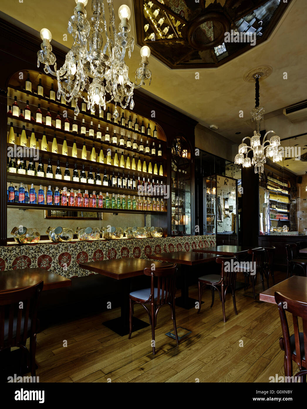 Ristorante René, Barcelona, Spagna. Scaffalature in legno rifornito con bottiglie. Lunga panca di legno con motivi il cuscino dello schienale e i tavoli e le sedie. Foto Stock