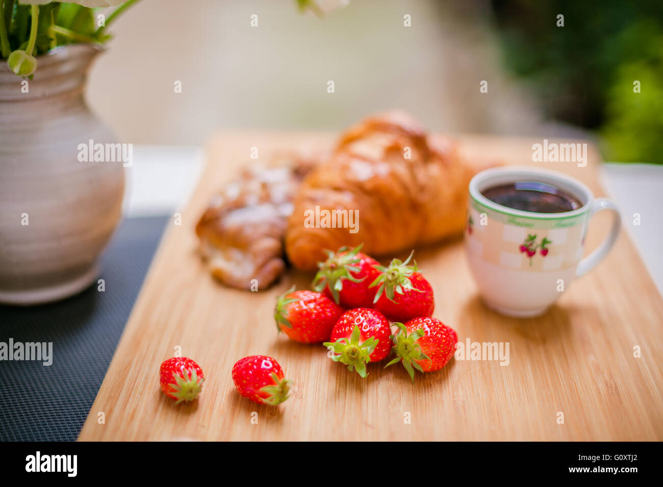 Morbido croissant francesi con bacche, una tazza di caffè e fiori freschi. Messa a fuoco selettiva. Foto Stock