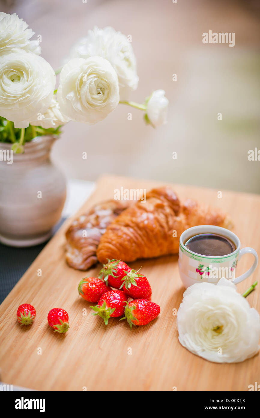 Morbido croissant francesi con bacche, una tazza di caffè e fiori freschi. Messa a fuoco selettiva. Foto Stock