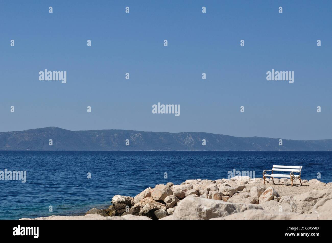 Banco di bianco in porto con pietre e cielo blu, isola Hvar in background. Podgora, Croazia. Spazio sul lato superiore Foto Stock